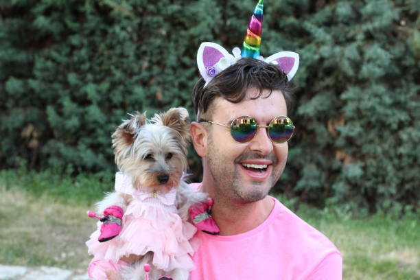 Joyful man and adorable Yorkie in colorful unicorn accessories outdoors.