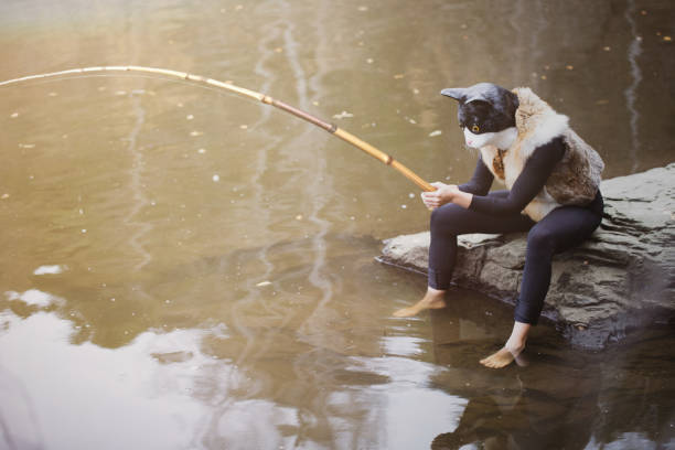 Whimsical cat-like fisherman sitting by water, fishing in a peaceful, natural setting with reflections.