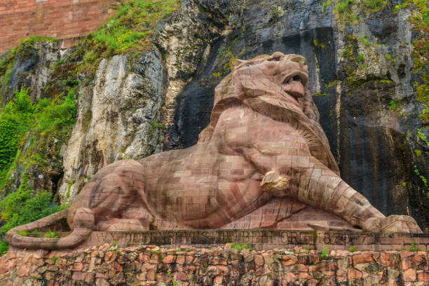 Stone lion sculpture in a natural rocky landscape with lush greenery and historical inscription.